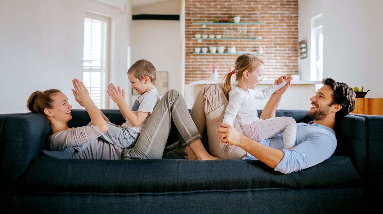 photo of a mother and father playing with their son and daughter on the couch