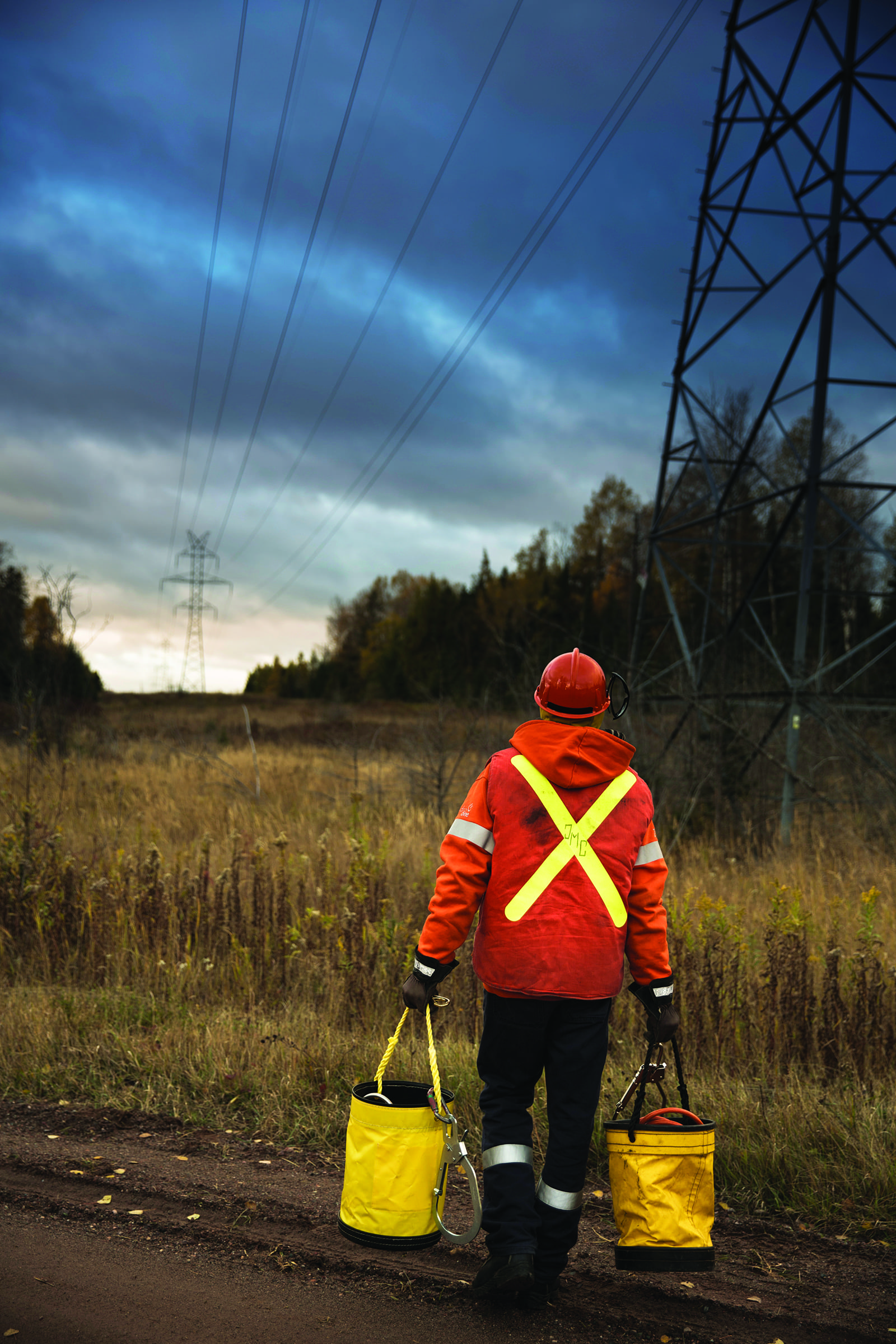 image of a Hydro One forestry management worker carrying equipment down a transmission right-of-way