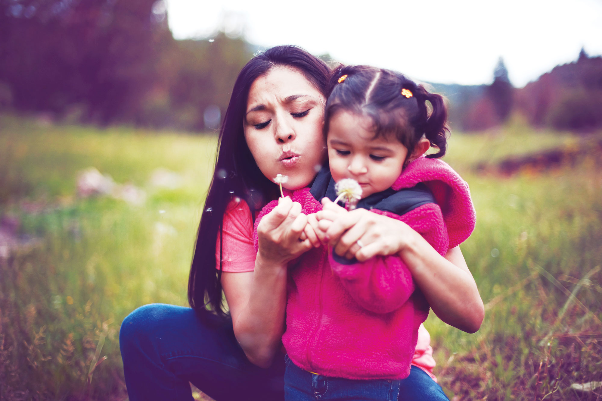 a mom and daughter blowing flowers in a field