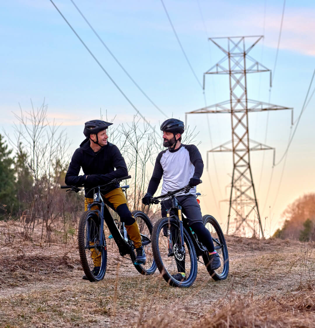 Two people on bikes talking in front of a transmission tower